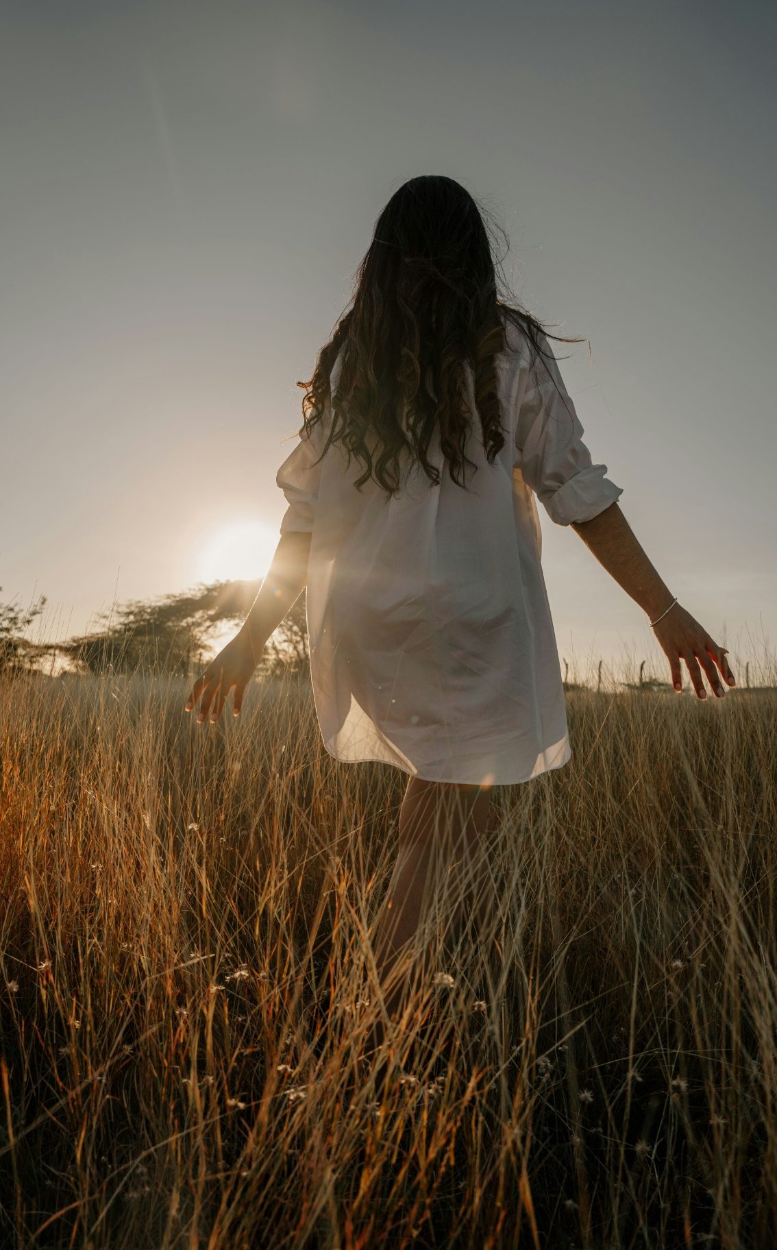 Femme marchant dans un champ doré sous un ciel ensoleillé.